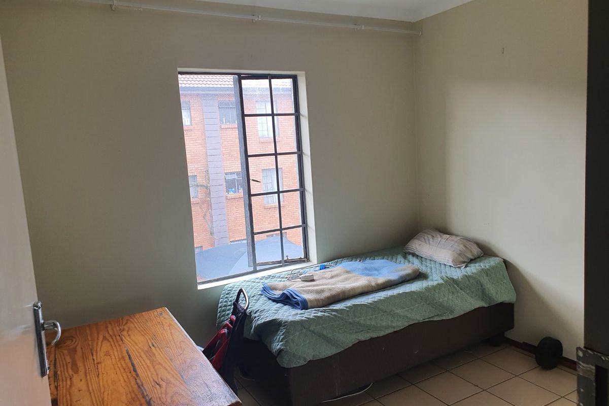 A simple bedroom featuring tiled flooring and a window with security bars, offering a functional space with potential for cosmetic updates.