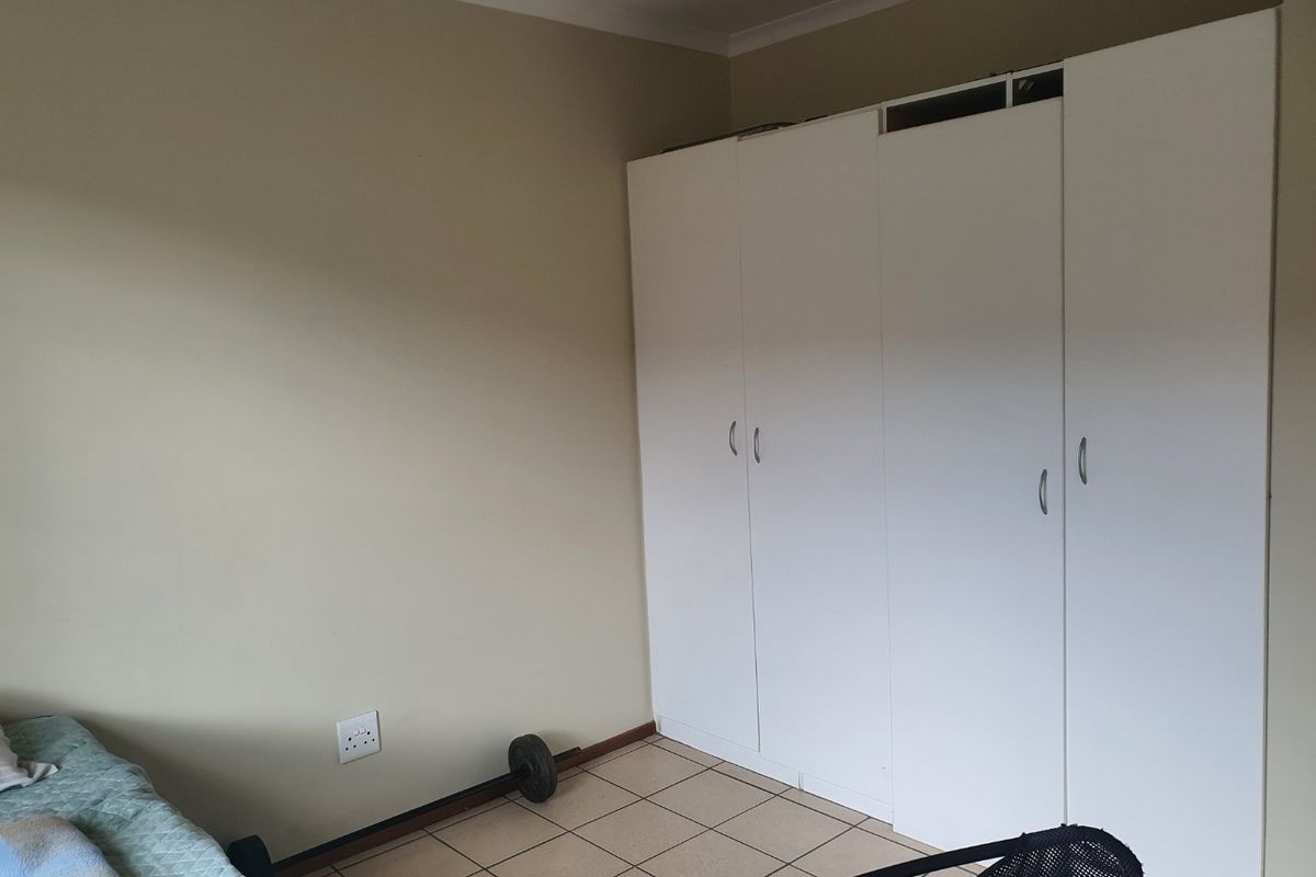 A bedroom featuring neutral wall paint, tiled flooring, and white built-in cupboards providing ample storage space.