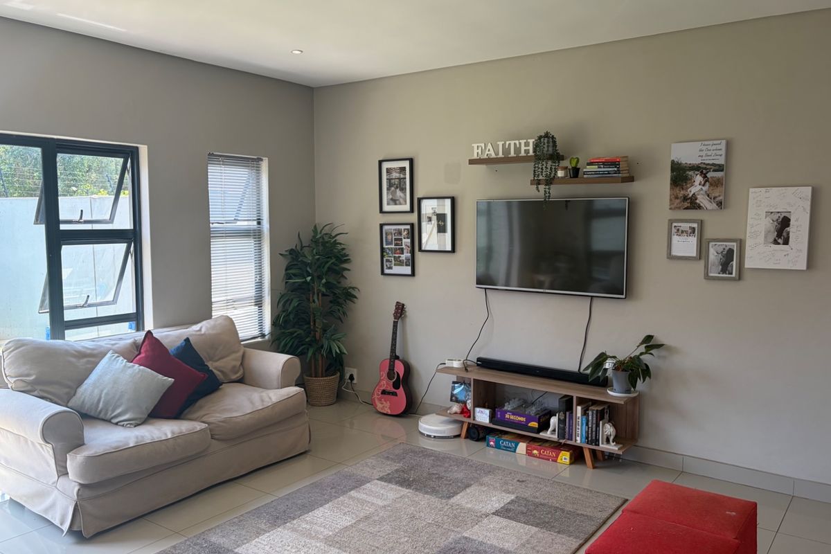 A well-maintained living room featuring neutral wall tones, tiled flooring, and modern aluminium window frames, providing a bright and comfortable living space.