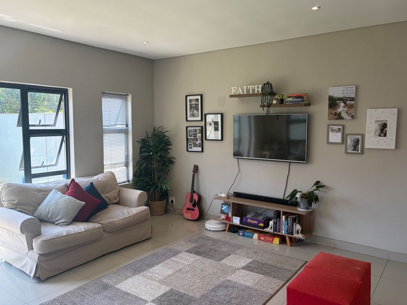 A well-maintained living room featuring neutral wall tones, tiled flooring, and modern aluminium window frames, providing a bright and comfortable living space.