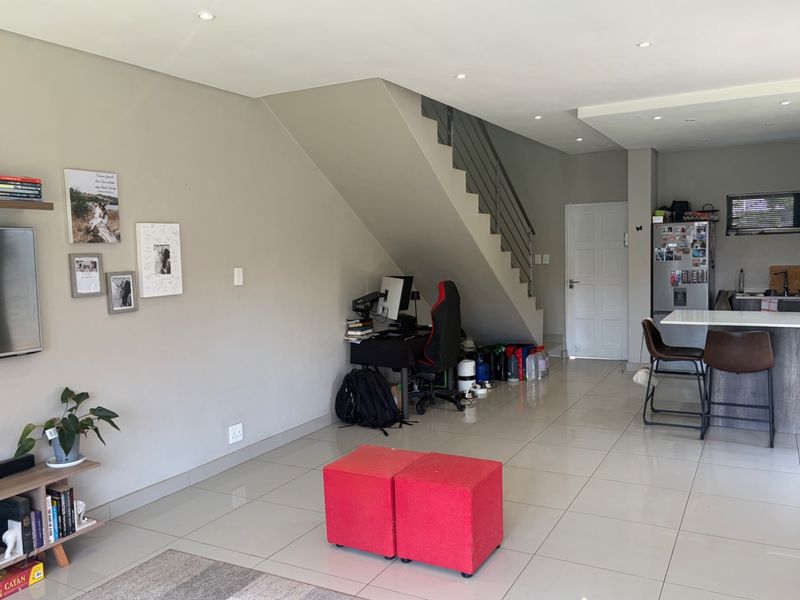 Open-plan living and kitchen area featuring tiled floors, recessed lighting, a modern staircase, and a functional kitchen island with stone countertops.