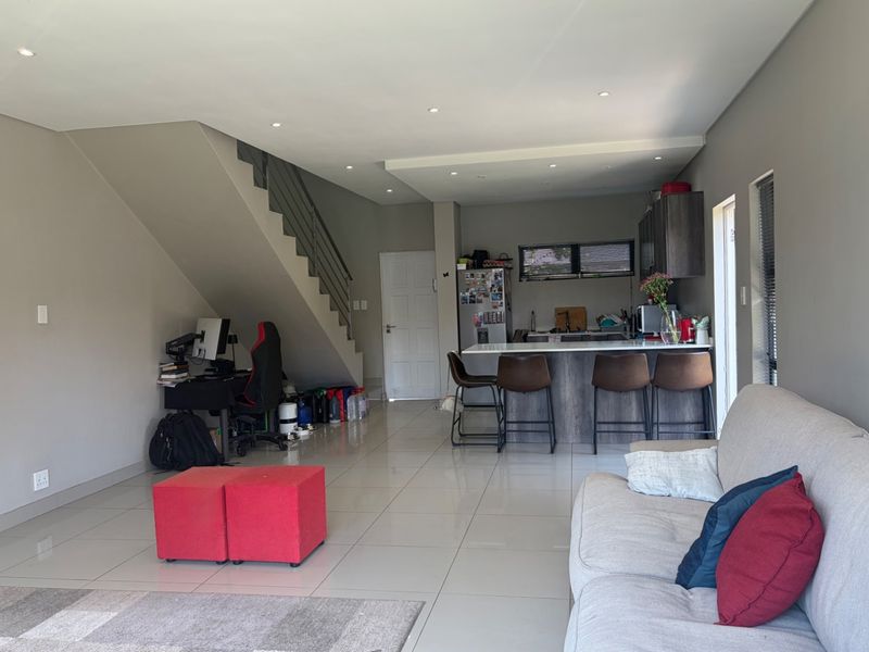 Open-plan living area featuring a modern kitchen with island, tiled flooring, recessed lighting, and an integrated staircase leading to the upper level.