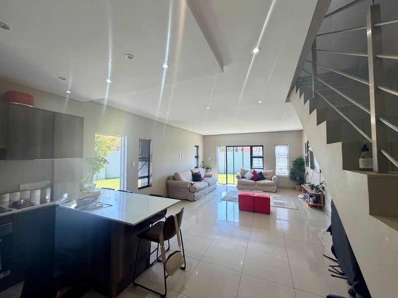 Spacious open-plan living area featuring a modern kitchen with island, tiled flooring, recessed lighting, and a staircase leading to the upper level.
