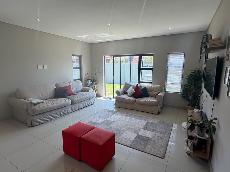 A bright and spacious living room featuring neutral tiled flooring, recessed downlighting, and large sliding glass doors providing direct access to the rear garden.
