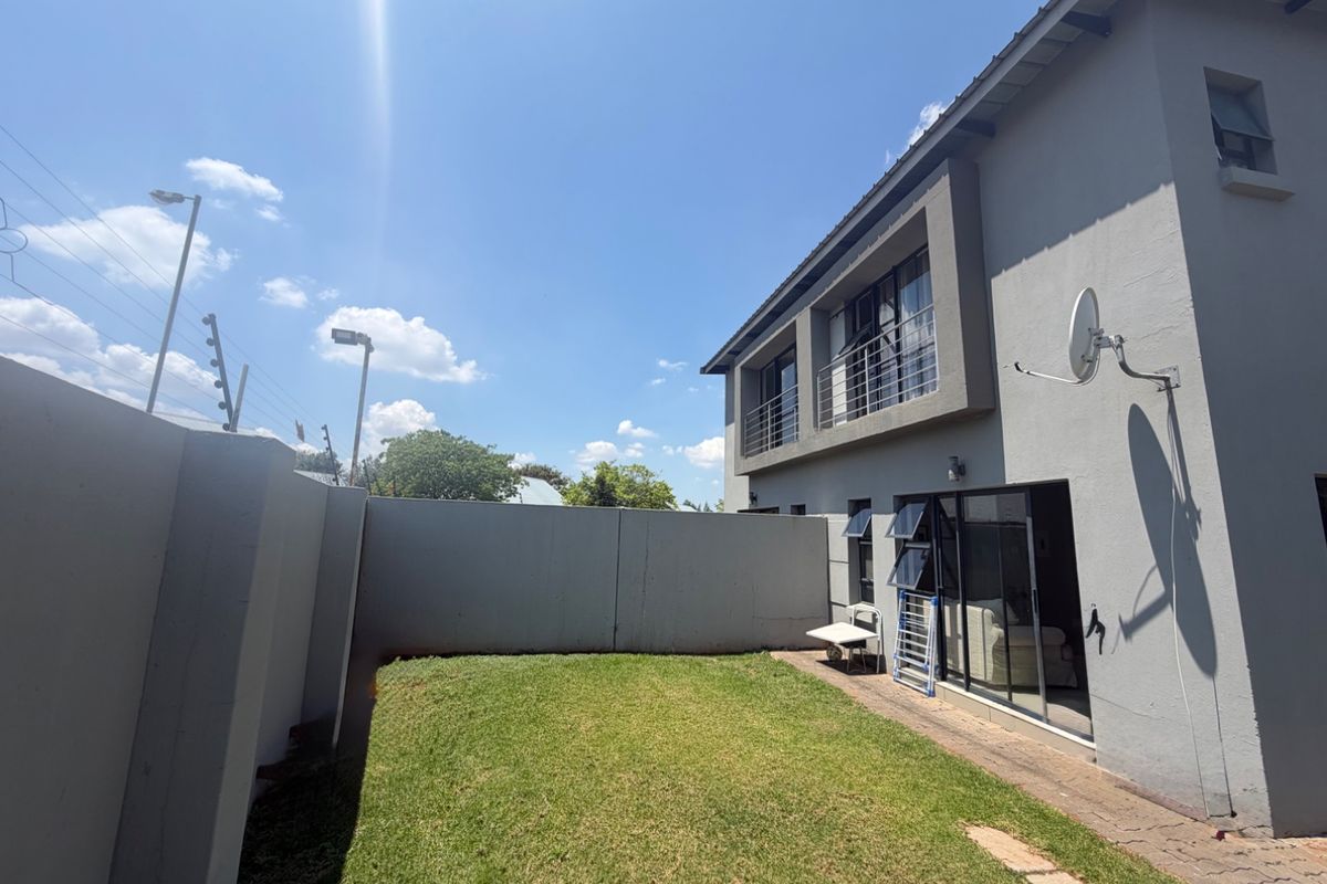 Rear view of the townhouse featuring a private garden, boundary wall with electric fencing, paved walkway, and a balcony on the upper level.