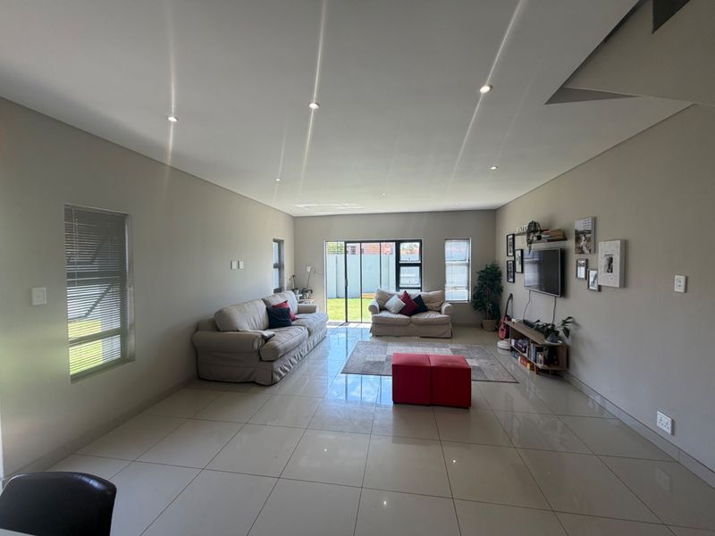 Spacious open-plan living area featuring large format floor tiles, recessed downlighting, and aluminium sliding doors providing direct access to the rear garden.
