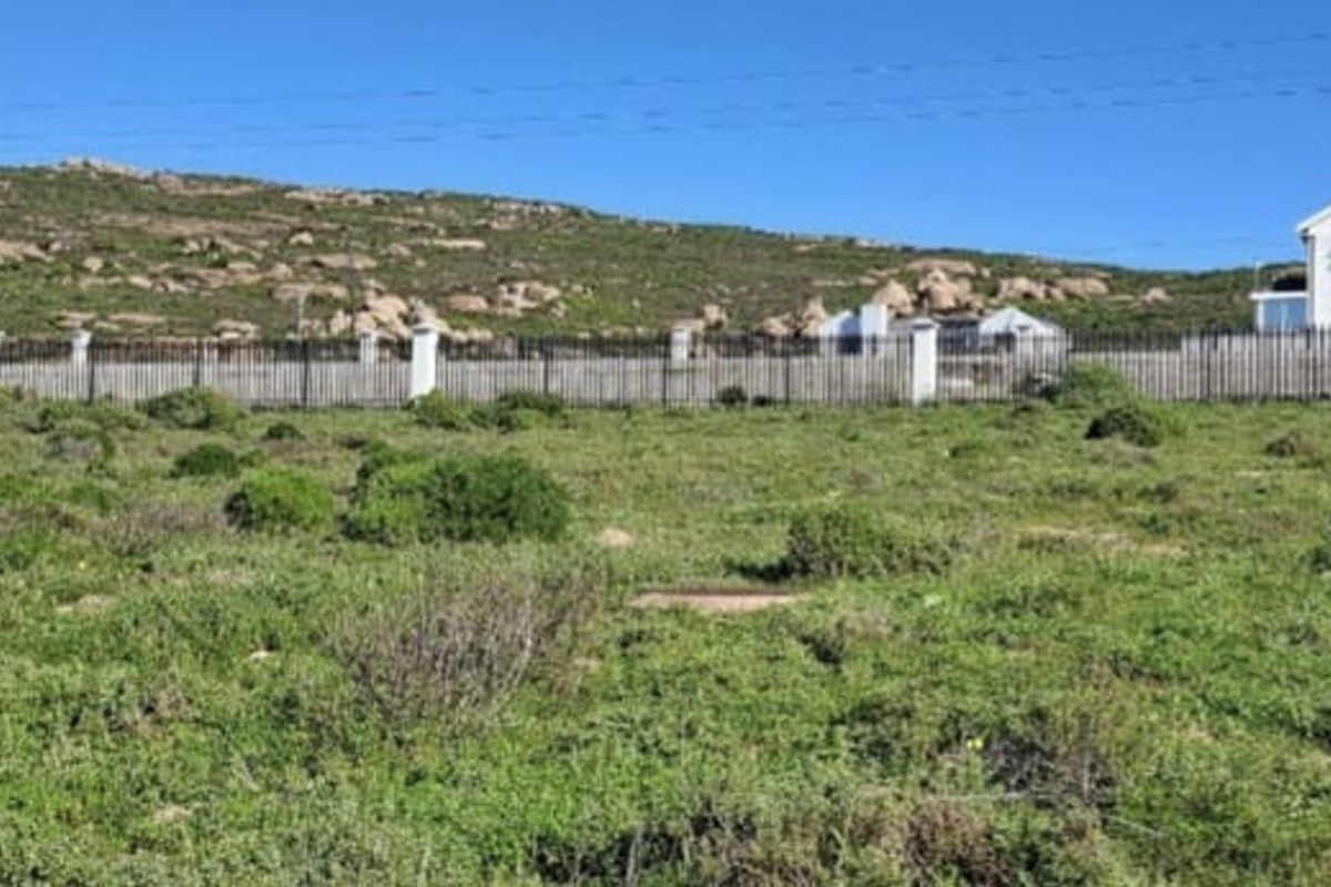 A view of a vacant residential plot featuring perimeter fencing with masonry pillars, set against a natural landscape and neighboring properties.