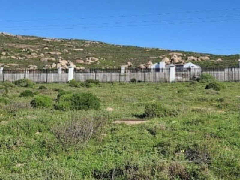 A view of a vacant residential plot featuring perimeter fencing with masonry pillars, set against a natural landscape and neighboring properties.