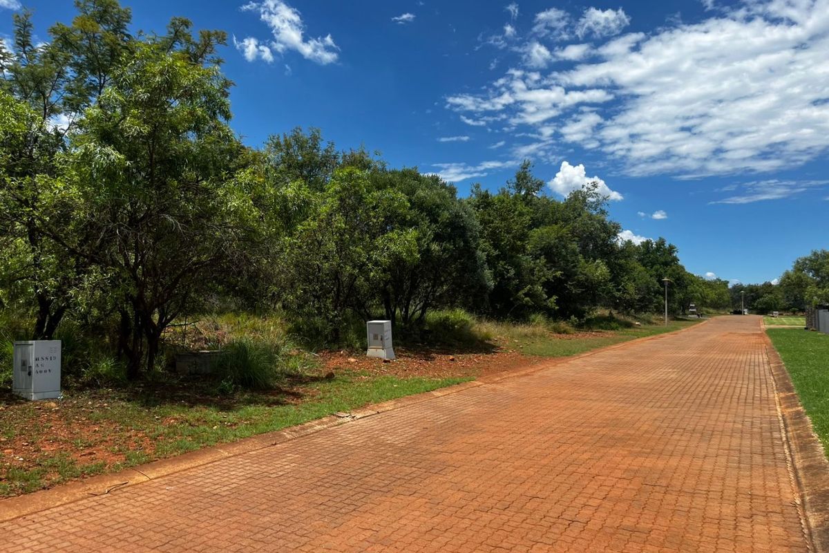 A view of a paved residential street with mature trees and utility infrastructure, showcasing the access and surroundings of the vacant land.