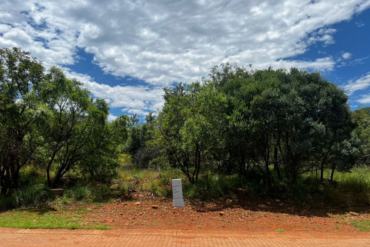A view of a vacant residential plot featuring mature trees and a survey marker, accessible from a paved road.