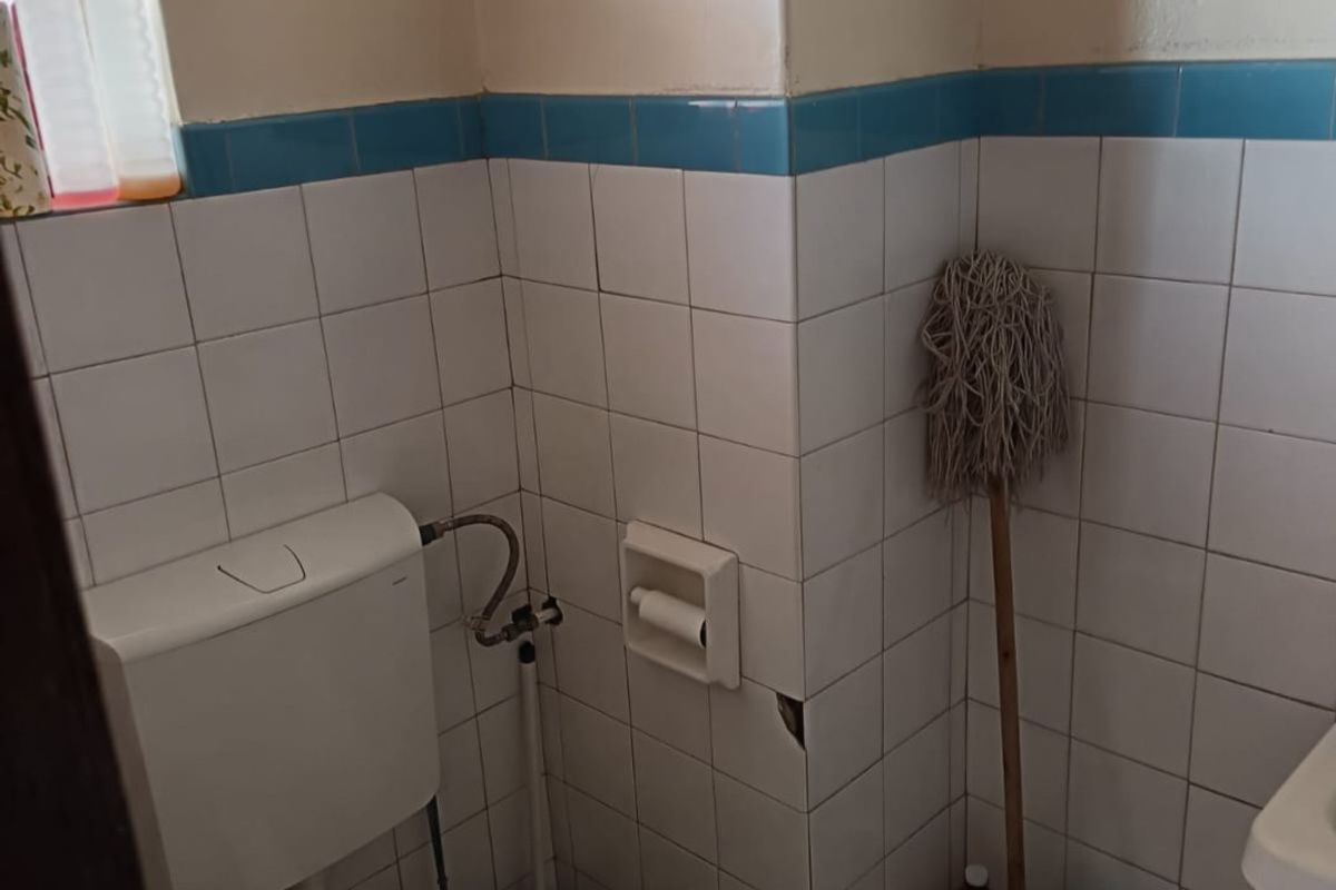 A compact bathroom featuring white wall tiles with a blue accent border, a standard toilet, and a built-in toilet roll holder.