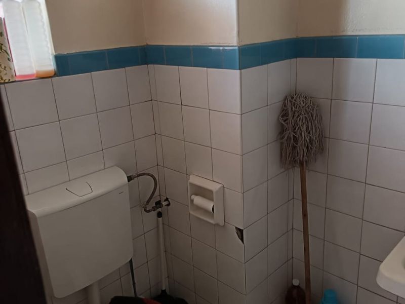 A compact bathroom featuring white wall tiles with a blue accent border, a standard toilet, and a built-in toilet roll holder.
