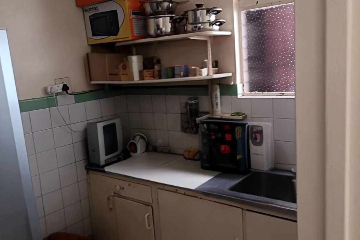 A compact kitchen featuring tiled splashbacks, built-in cabinetry, and a stainless steel sink, offering a functional space with potential for modernization.