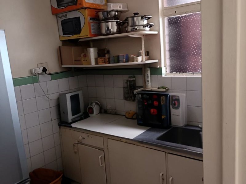 A compact kitchen featuring tiled splashbacks, built-in cabinetry, and a stainless steel sink, offering a functional space with potential for modernization.