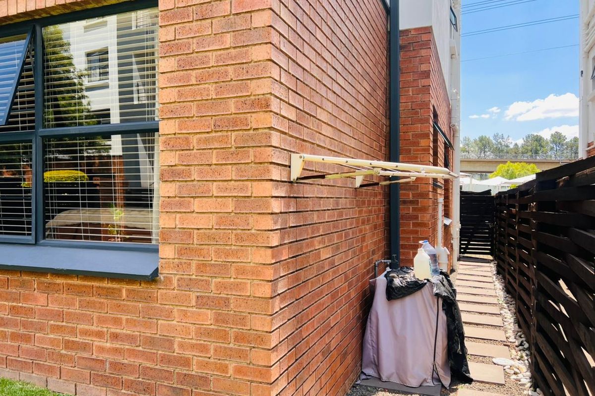 A side exterior view of the apartment featuring face brick walls, an aluminium window, and a wall-mounted drying rack over a paved walkway.