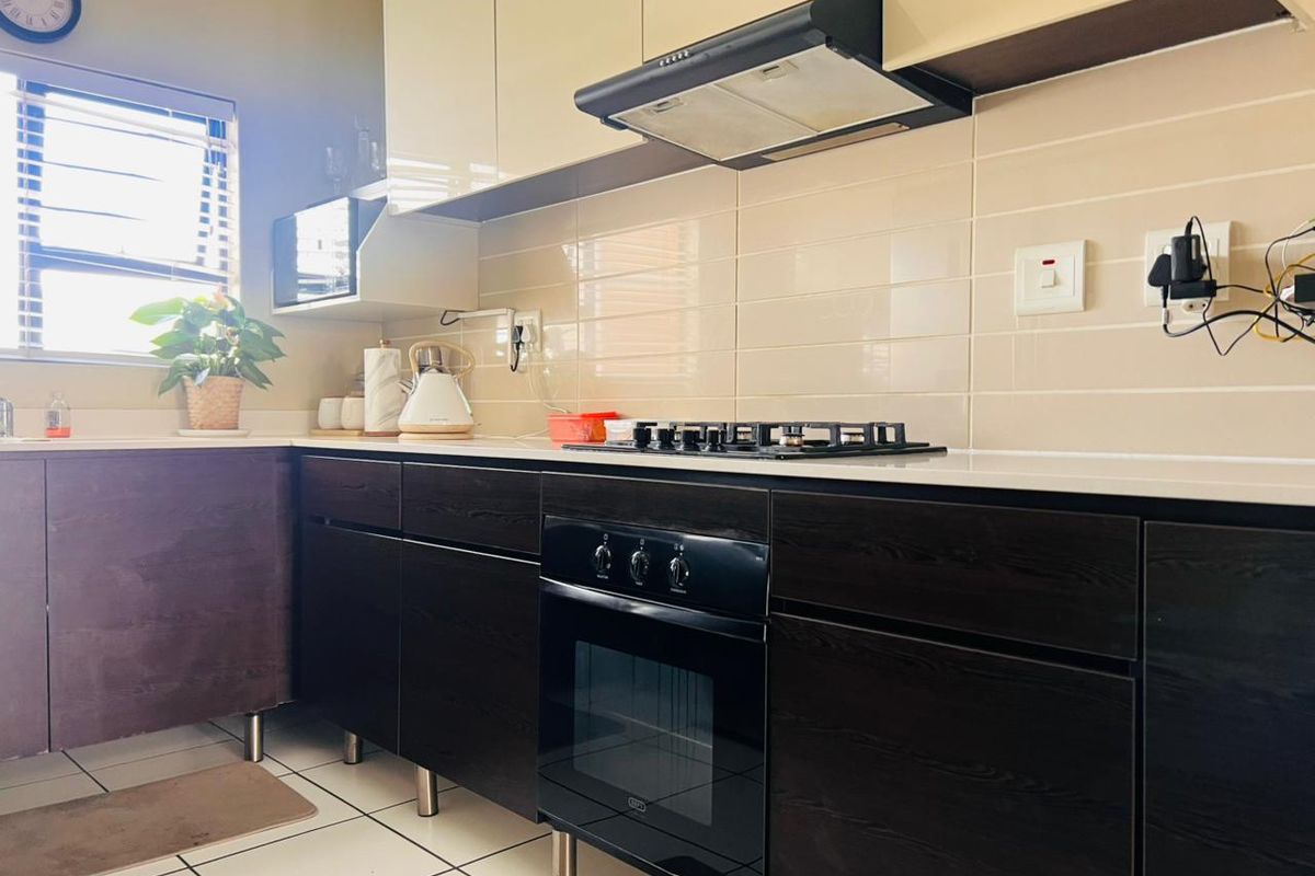 Modern kitchen featuring dark wood lower cabinetry, high-gloss upper cabinets, gas hob, built-in oven, extractor fan, and tiled backsplash.