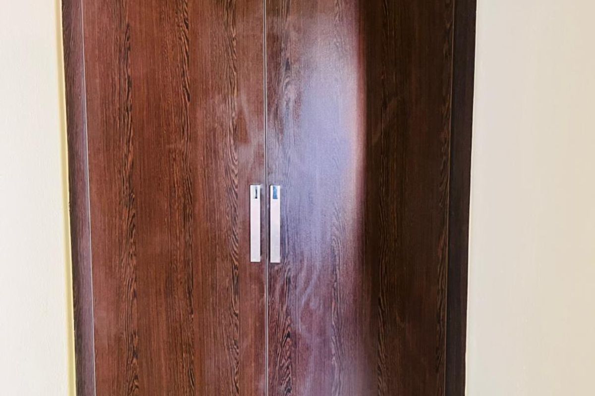 A close-up view of a built-in bedroom wardrobe featuring a dark wood-grain finish and modern metal handles.
