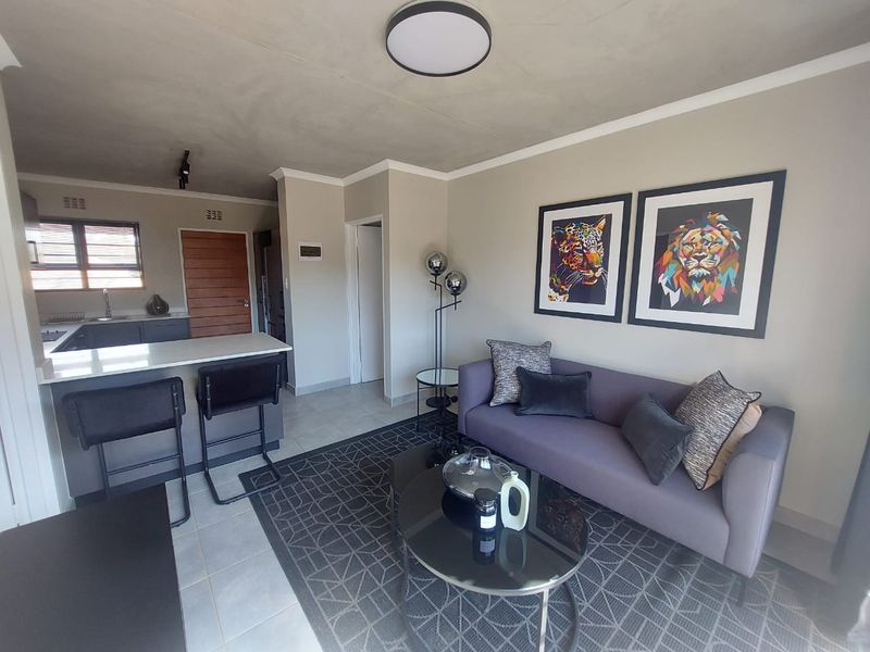 Modern open-plan living area featuring a functional kitchen with stone countertops and tiled flooring, seamlessly flowing into a comfortable lounge space.