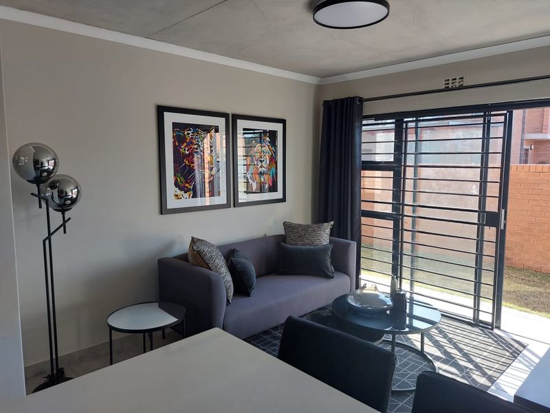 A modern living room featuring an exposed concrete ceiling, neutral walls, and a large sliding glass door with security gate leading to the exterior.