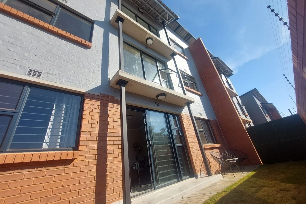 Rear view of a multi-story apartment building featuring brick and painted masonry facade, sliding glass doors, and a paved patio area.