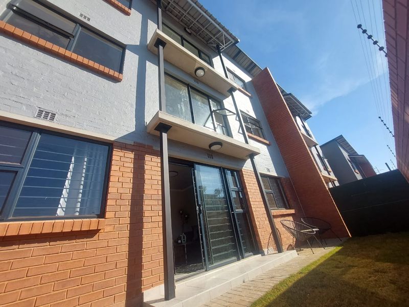 Rear view of a multi-story apartment building featuring brick and painted masonry facade, sliding glass doors, and a paved patio area.