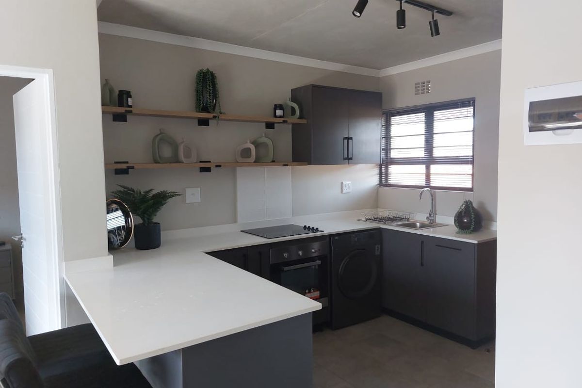 Modern kitchen featuring dark cabinetry, white quartz countertops, built-in oven, electric hob, integrated washing machine, and stylish open shelving.