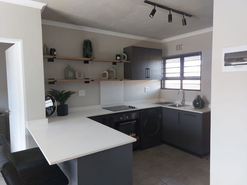Modern kitchen featuring dark cabinetry, white quartz countertops, built-in oven, electric hob, integrated washing machine, and stylish open shelving.