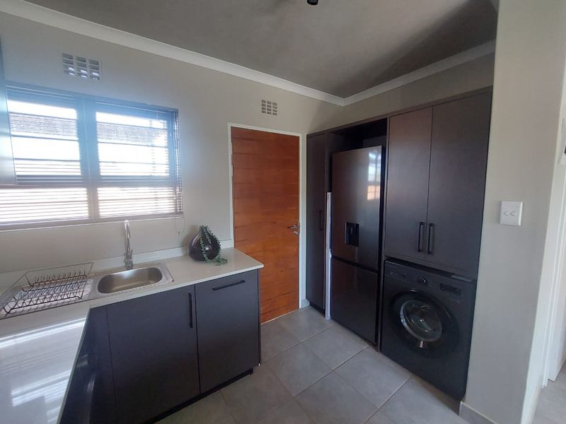 Modern kitchen featuring dark cabinetry, stone countertops, integrated appliances, and tiled flooring with a functional layout.