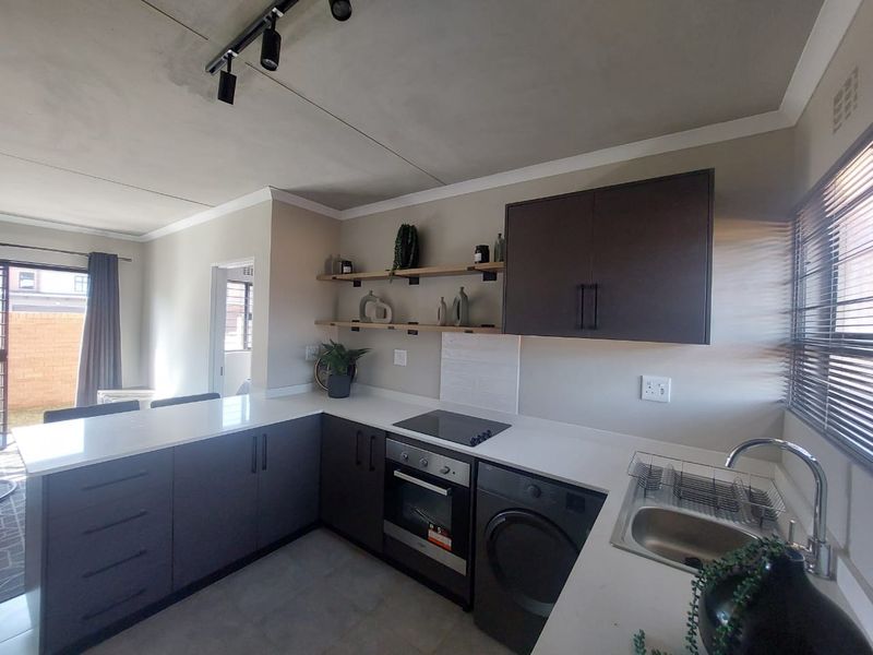 Modern kitchen featuring dark cabinetry, white quartz countertops, built-in oven and hob, integrated washing machine, and stylish floating shelving.