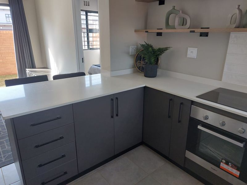 Modern kitchen featuring grey cabinetry, white quartz countertops, built-in oven, electric hob, and open floating shelving with a tiled backsplash.