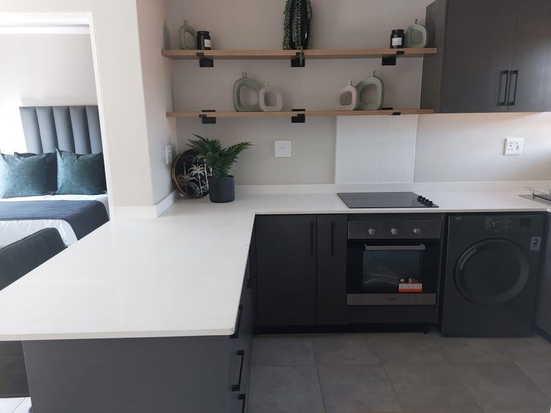Modern kitchen featuring dark cabinetry, quartz countertops, built-in oven, electric hob, and integrated washing machine, with open shelving and tiled flooring.