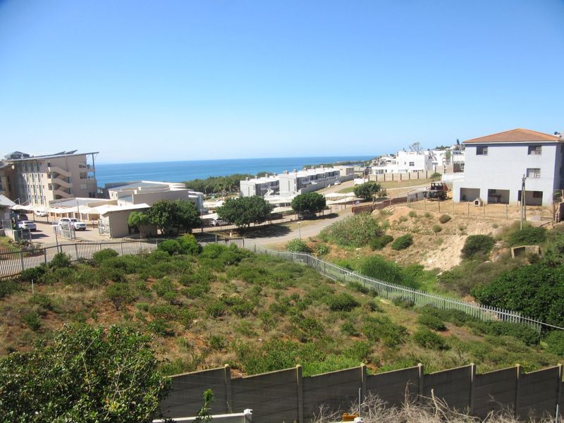 An elevated view overlooking a vacant residential plot with coastal scenery and surrounding neighborhood infrastructure in the distance.