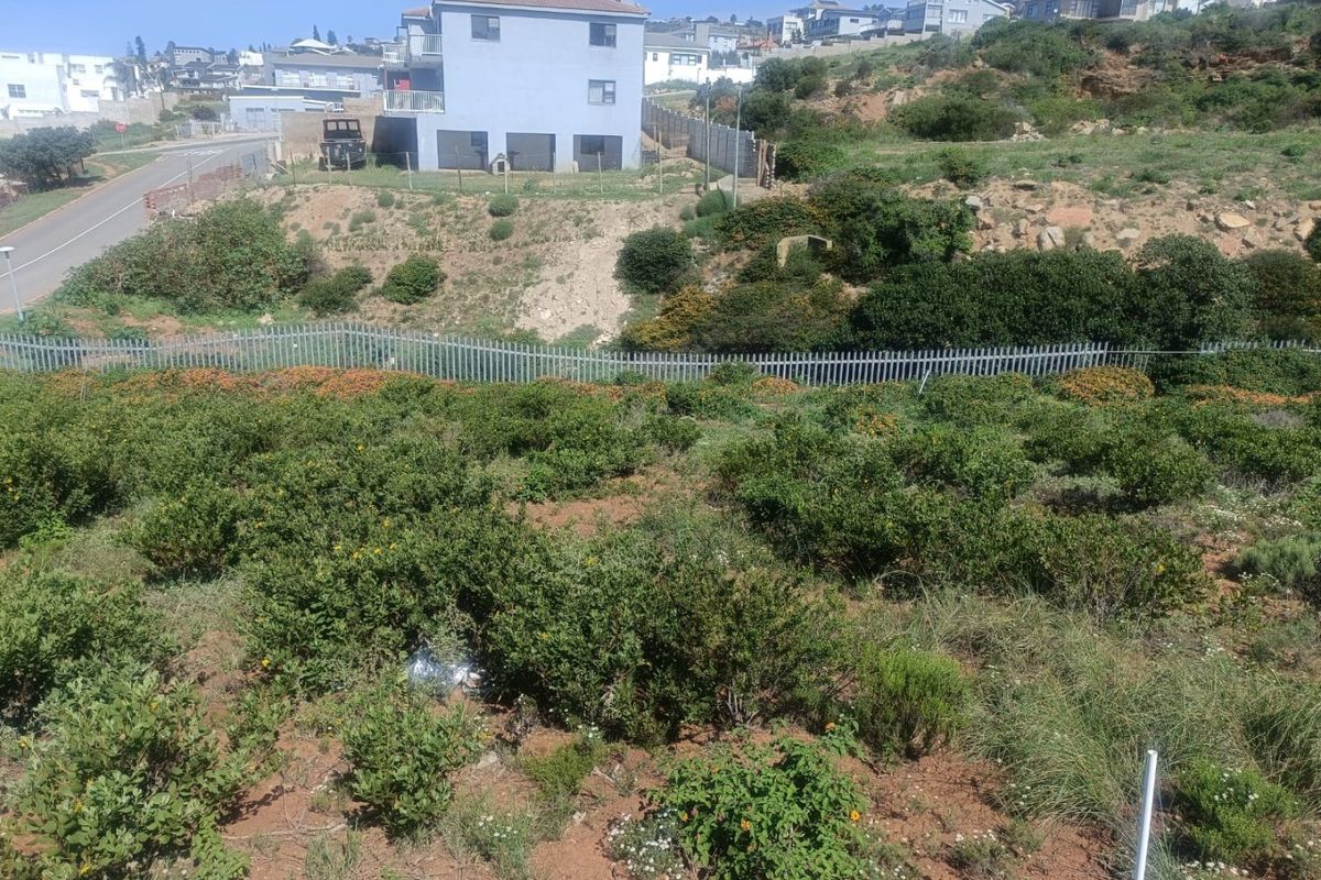 A view of a vacant residential plot featuring sloped terrain and perimeter fencing, situated in a developed suburban neighborhood.