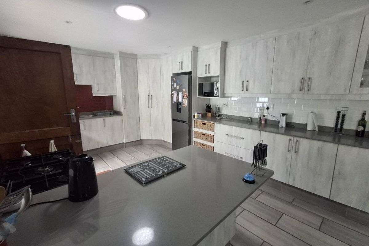 A functional kitchen featuring light wood-grain cabinetry, stone countertops, a central island, and a subway tile backsplash with integrated appliances.