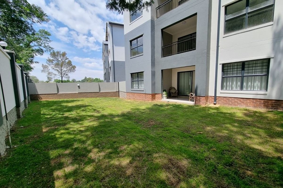 A view of the rear exterior of the apartment building, featuring a private lawn area, boundary wall, and balconies with metal railings.