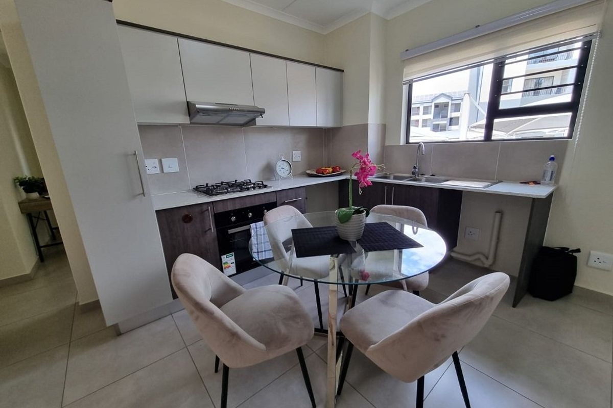 Modern kitchen featuring built-in cabinetry, stone countertops, gas hob, electric oven, and stainless steel sink, with tiled flooring and ample natural light.
