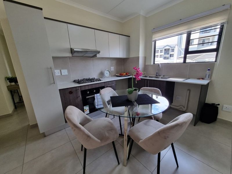 Modern kitchen featuring built-in cabinetry, stone countertops, gas hob, electric oven, and stainless steel sink, with tiled flooring and ample natural light.