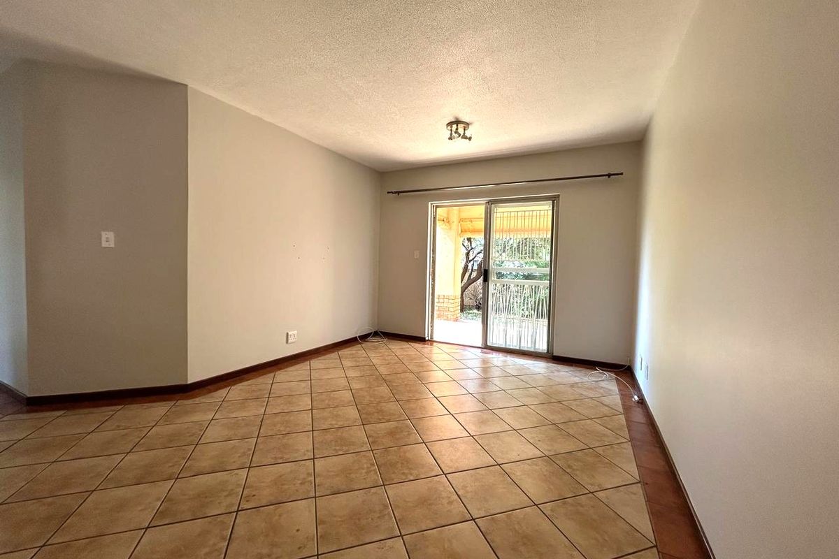 An empty living room featuring neutral tiled flooring and a sliding glass door providing access to the outdoor area.