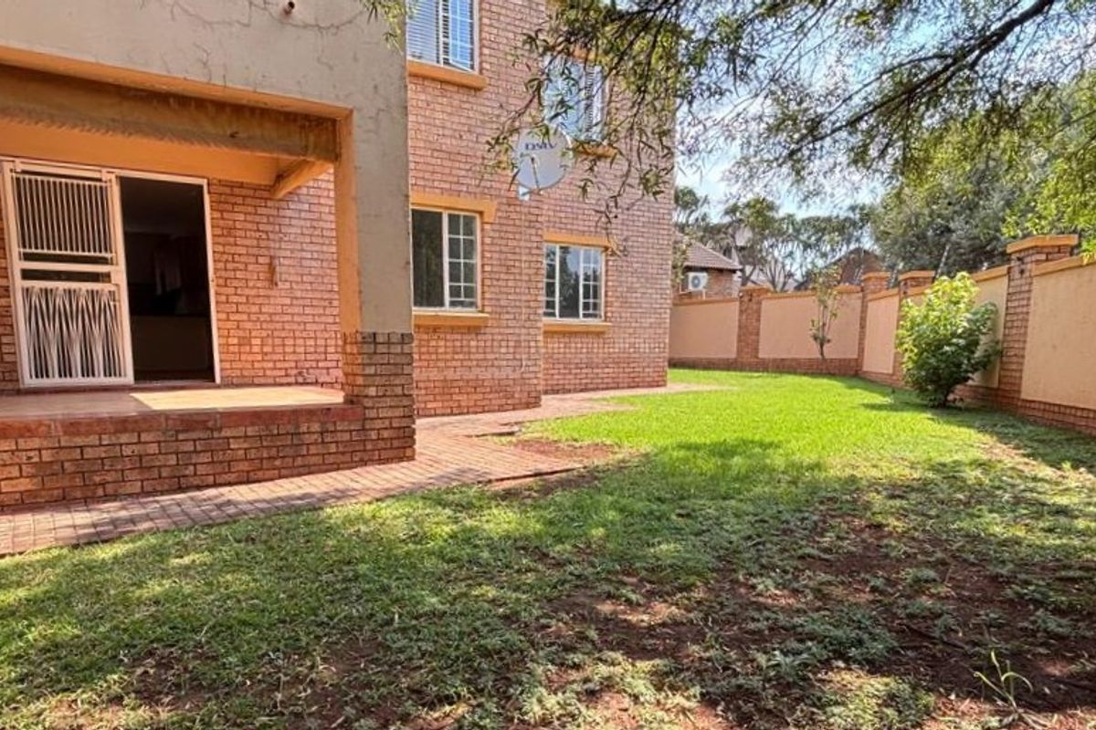 Rear view of the apartment featuring a covered patio, brick facade, and a private garden area enclosed by a perimeter wall.