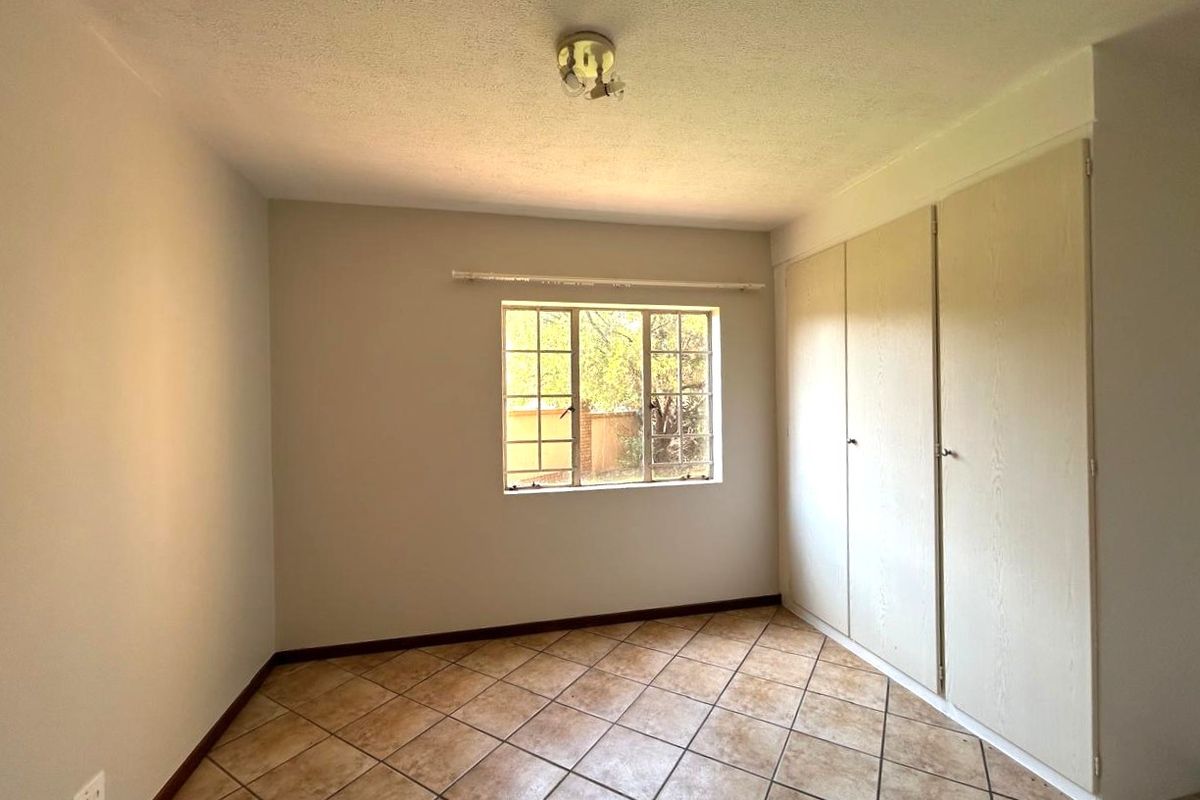 A vacant bedroom featuring tiled flooring, built-in cupboards, and a window with security bars, offering a neutral canvas for potential updates.