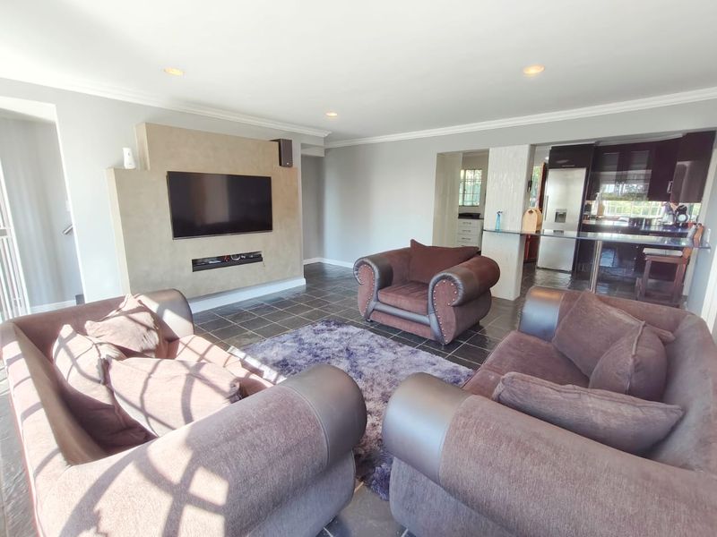 Spacious open-plan living area featuring a modern built-in media wall, stone tile flooring, and a seamless transition into the adjacent kitchen space.