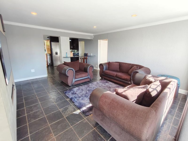 Open-plan living area featuring dark slate tile flooring, recessed lighting, and a built-in fireplace, flowing into a functional kitchen space.