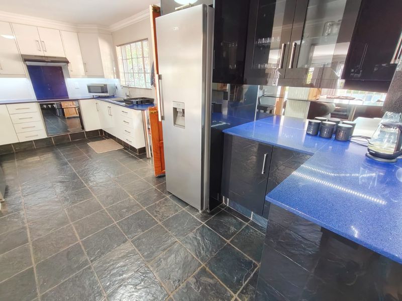 A functional kitchen featuring contrasting white and black cabinetry, vibrant blue stone countertops, integrated appliances, and durable slate tile flooring.