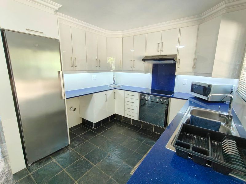 Modern kitchen featuring high-gloss white cabinetry, blue stone countertops, integrated appliances, and dark slate floor tiles with under-cabinet lighting.
