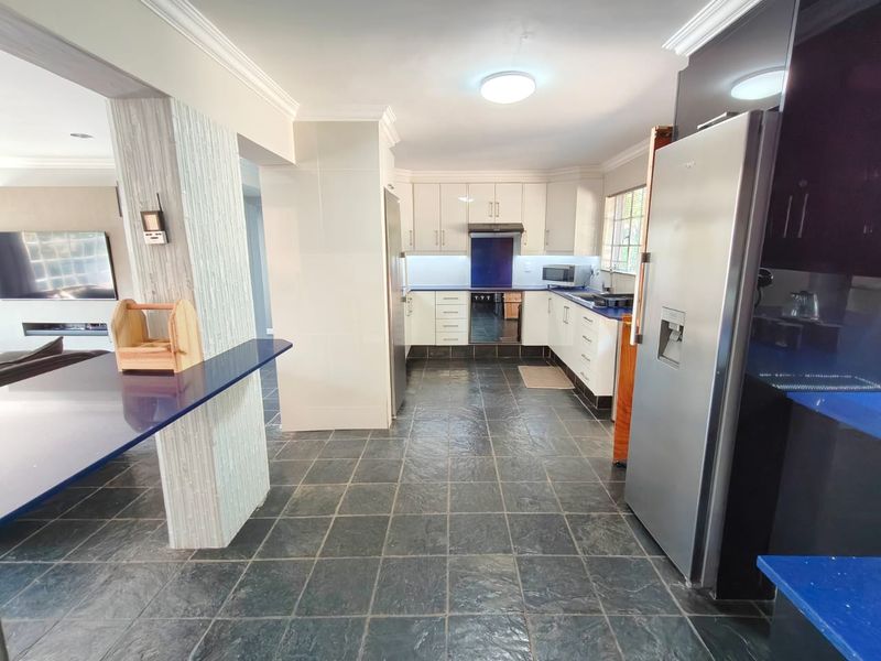 A well-maintained kitchen featuring dark slate flooring, white cabinetry, and contrasting blue countertops, seamlessly flowing into the adjacent living area.
