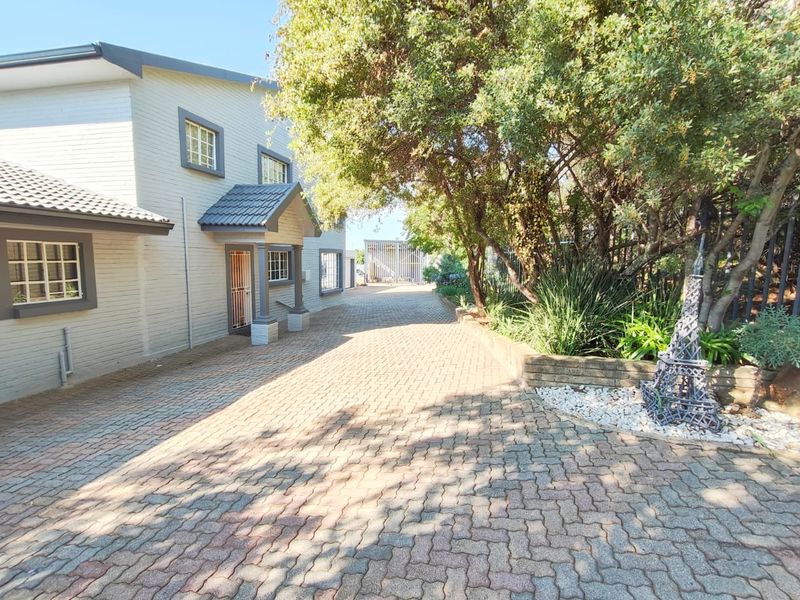 A paved driveway leading to the front entrance of a brick house, featuring mature trees and a retaining wall.
