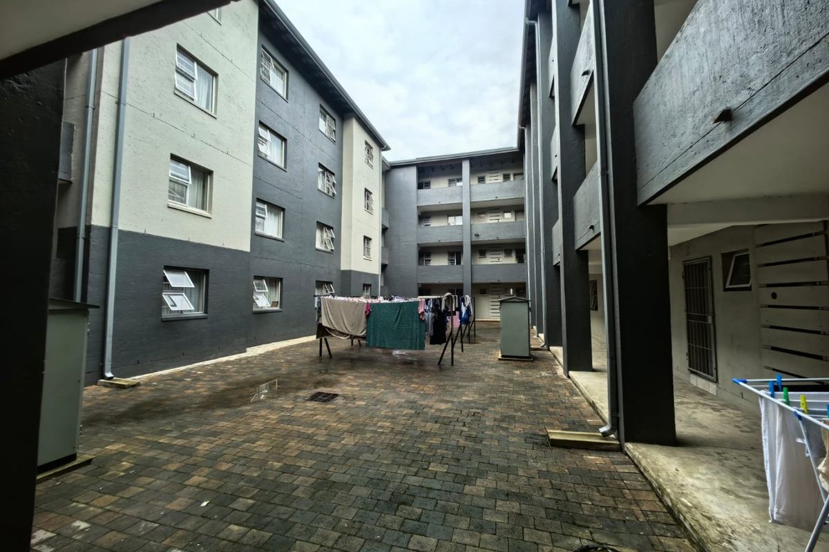 A view of the paved communal courtyard area between apartment building blocks, featuring multi-story facades and drainage infrastructure.