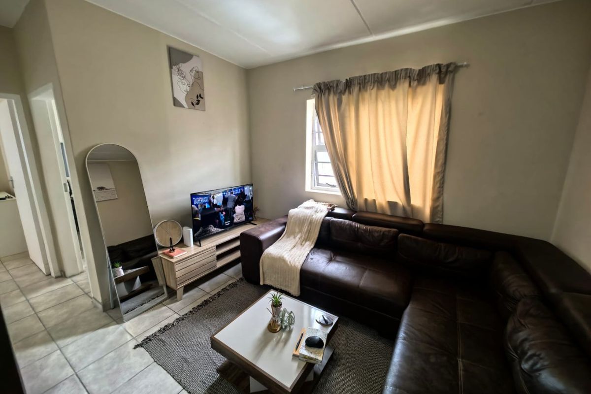 A comfortable living room featuring tiled flooring and a window with a curtain rod, providing a functional and well-lit space.