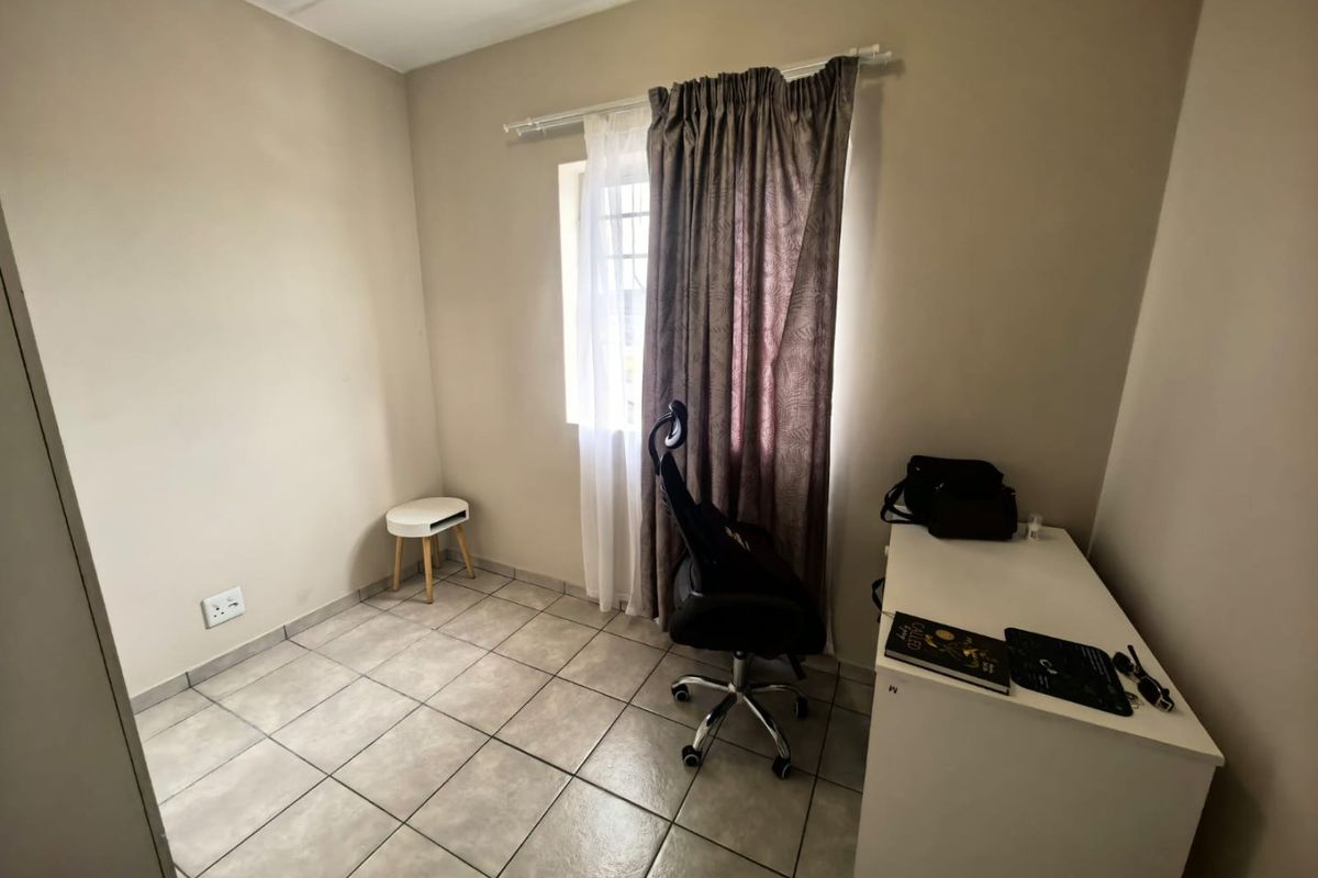 A compact bedroom featuring neutral wall paint, tiled flooring, and a window with installed curtain rods, providing a functional space for a bedroom or office.