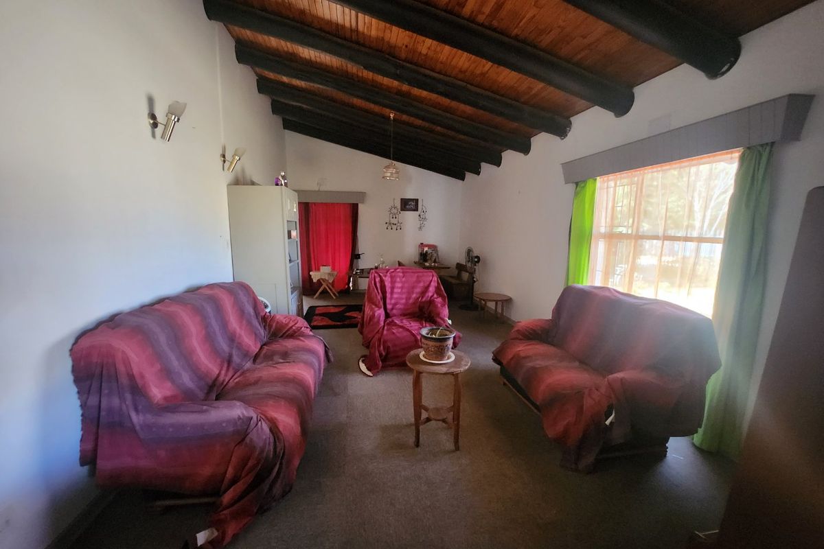 A living room featuring a high raked timber-beamed ceiling and large windows, offering a spacious layout with potential for modernization.